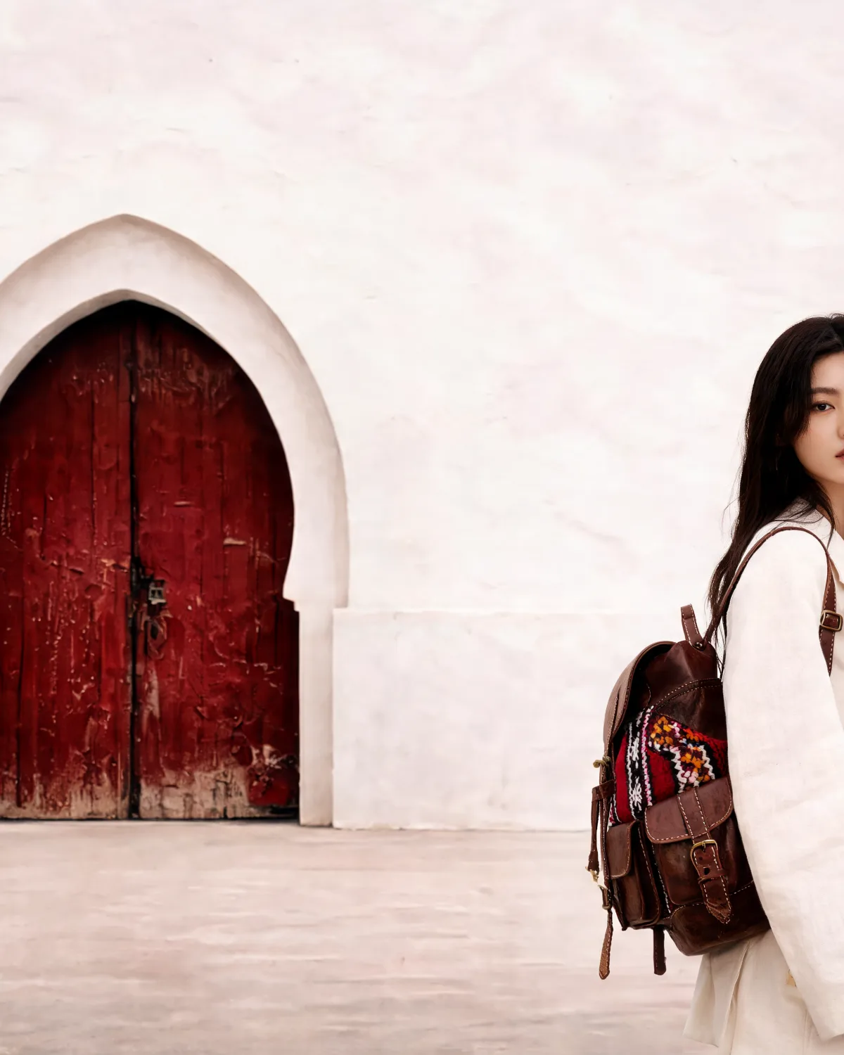 The kilim rucksack carried past a deep-red carved door in a whitewashed medina wall